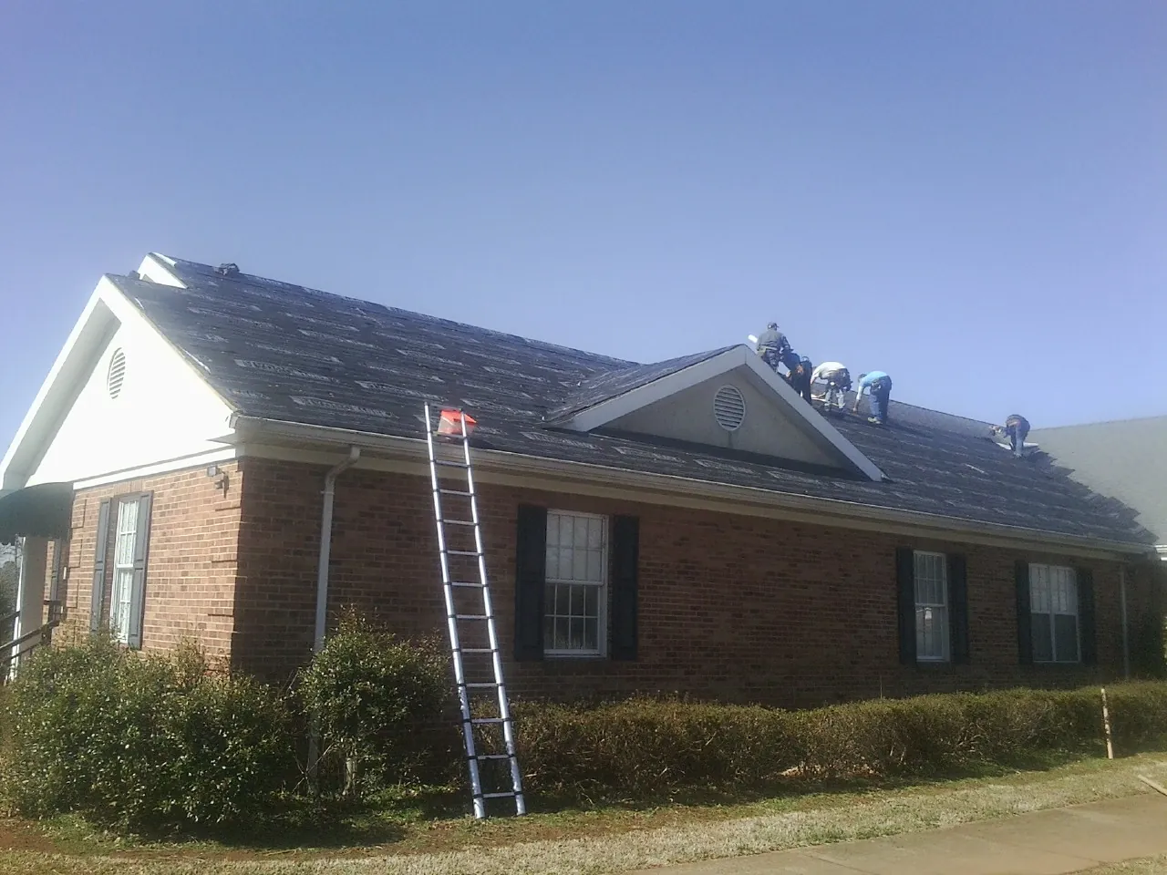 Crew tearing shingles off a brick ranch roof with a ladder set — Metal Roof Repair work by our crew in Gulf Shores