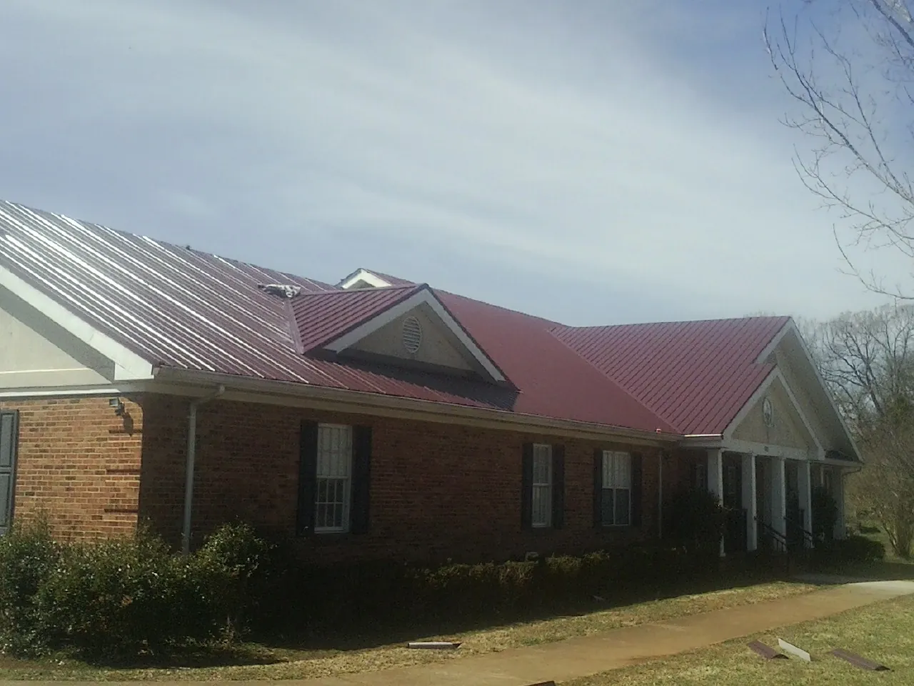 Red metal roof with gabled entries on a long brick building, from a Hail Damage Roof Repair job in Gulf Shores
