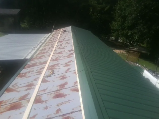 Old rusted panels beside newly installed green metal roofing — Wind Damage Roof Repair by Roofing Brothers in Gulf Shores