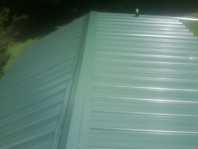 New green metal panels meeting at the ridge of a roof — Flat Roof Repair work by our crew in Gulf Shores