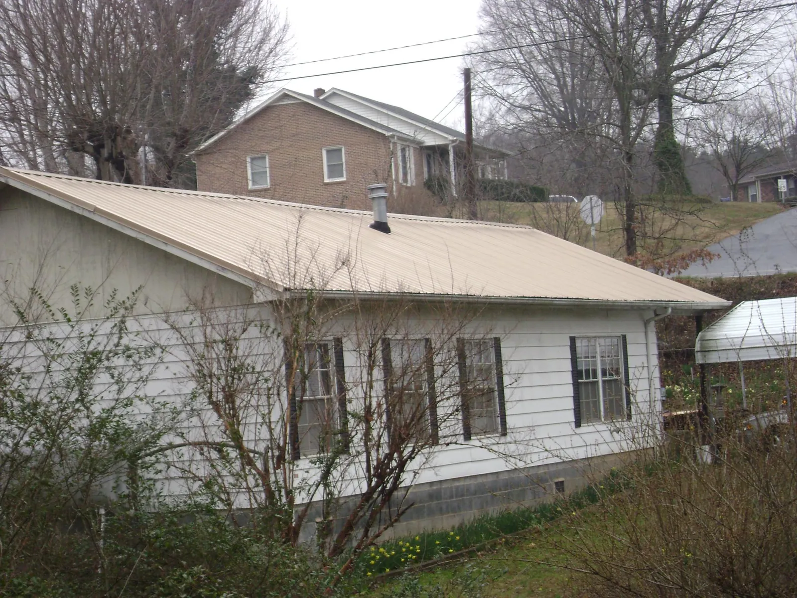 Tan metal roof on a white sided house set into a hillside — Commercial Roofing by Roofing Brothers in Gulf Shores