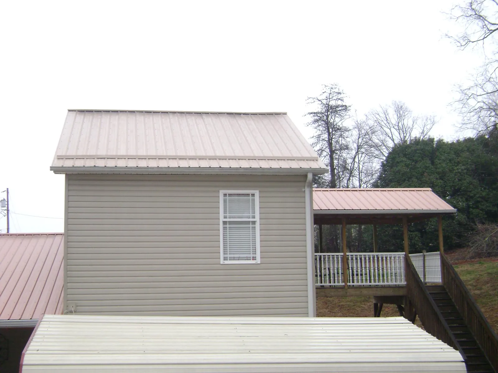 Tan metal roofs on a two story addition and attached porch, from a Roof Replacement job in Gulf Shores